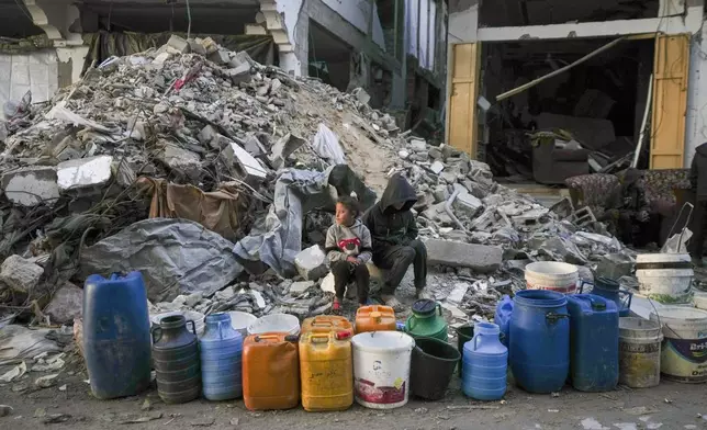 Two children wait to get water next to a line of empty jerrycans in an area largely destroyed by the Israeli army's air and ground offensive in Gaza City, Gaza Strip, Wednesday, Feb. 5, 2025. (AP Photo/Abdel Kareem Hana)