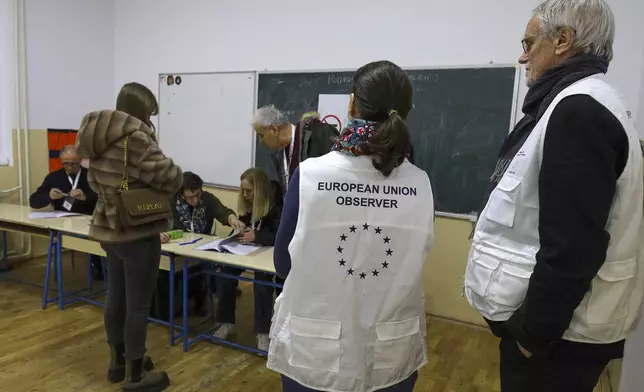 European Union election observers watch a voter at a polling station during a parliamentary election in the northern Serb-dominated part of ethnically divided town of Mitrovica, Kosovo, Sunday, Feb. 9, 2025. (AP Photo/Bojan Slavkovic)