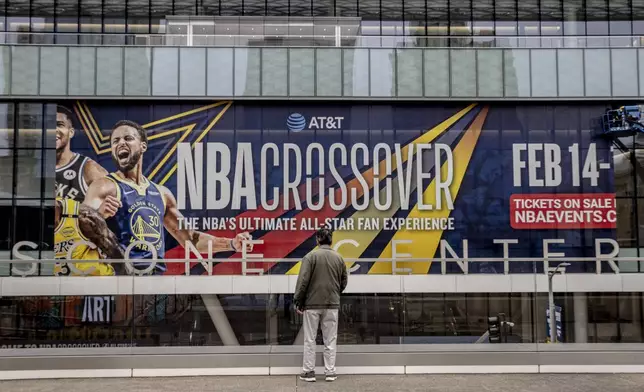A pedestrian watches a window decal being installed outside Moscone Center ahead of the NBA All-Star Weekend in San Francisco, Tuesday, Feb. 11, 2025. (Stephen Lam/San Francisco Chronicle via AP)