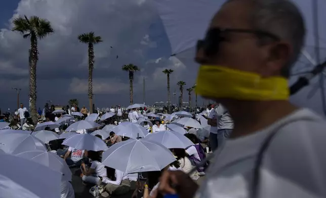 Activists sit on a road with white umbrellas during a protest calling for the release of hostages held in the Gaza Strip, in front of the U.S. Embassy branch office in Tel Aviv, Israel, Friday, Jan. 31, 2025. (AP Photo/Oded Balilty)