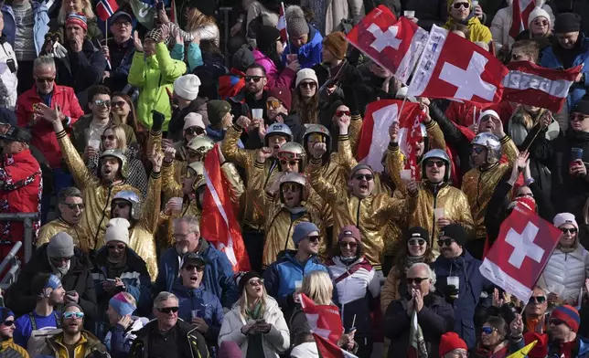 Spectators wearing golden jackets and shiny helmets cheer in the crowd at the finish area of a men's downhill race, at the Alpine Ski World Championships, in Saalbach-Hinterglemm, Austria, Sunday, Feb. 9, 2025. (AP Photo/Giovanni Auletta)