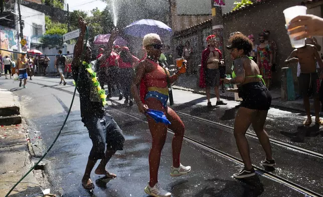A reveler sprays water on fellow merry makers cooling them off during the "Ceu na Terra" or "Heaven on Earth" pre-Carnival street party, amid a heat wave in Rio de Janeiro, Saturday, Feb. 22, 2025. (AP Photo/Bruna Prado)