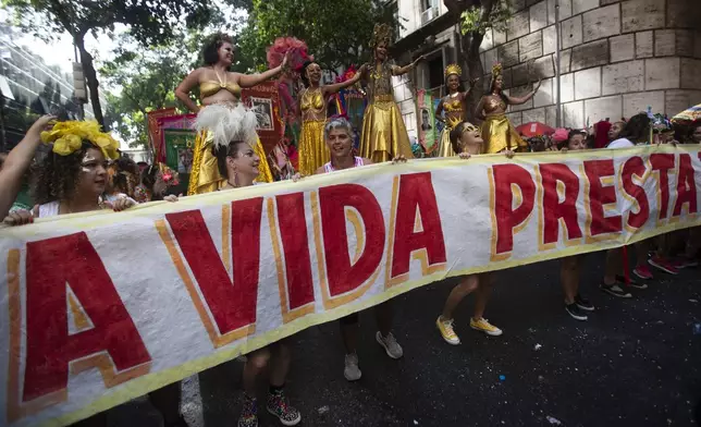 Revelers hold a banner that reads in Portuguese, "Life is worth it," to pay tribute to Brazilian actress Fernanda Torres during the "Cordao do Boitata" street pre-carnival party in Rio de Janeiro, Sunday, Feb. 23, 2025. (AP Photo/Bruna Prado)