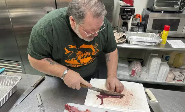 Sam Bohr cuts raw coyote meat before it was cooked and served at a wild game dinner in Pine Grove, Pa., on Saturday, Feb. 15, 2025. (AP Photo/Mark Scolforo)