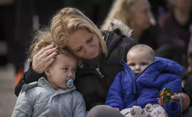 A woman holds two children at Hostage Square in Tel Aviv, Israel, Thursday, Feb. 20, 2025, after Palestinian militant groups handed over four bodies to the Red Cross in Gaza. Israel has identified three of the bodies as hostages and said the other was of an unknown person. (AP Photo/Oded Balilty)