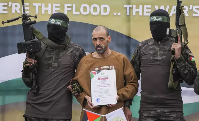 Israeli captive, Eli Sharabi, who has been held hostage by Hamas in Gaza since October 7, 2023, stands on a stage escorted by Hamas fighters before being handed over to the Red Cross in Deir al-Balah, central Gaza Strip, Saturday Feb. 8, 2025. (AP Photo/Abdel Kareem Hana)