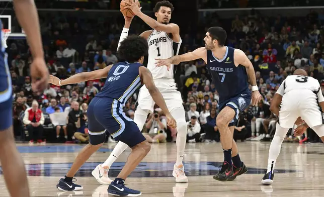 San Antonio Spurs center Victor Wembanyama (1) handles the ball between Memphis Grizzlies forwards Jaylen Wells (0) and Santi Aldama (7) in the first half of an NBA basketball game Monday, Feb. 3, 2025, in Memphis, Tenn. (AP Photo/Brandon Dill)
