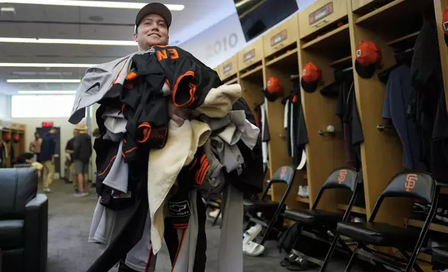 San Francisco Giants clubhouse attendant Riley Halpin gathers a mound of dirty clothes in the clubhouse after spring training baseball practice at the team's facility, Monday, Feb. 17, 2025, in Scottsdale, Ariz. (AP Photo/Carolyn Kaster)
