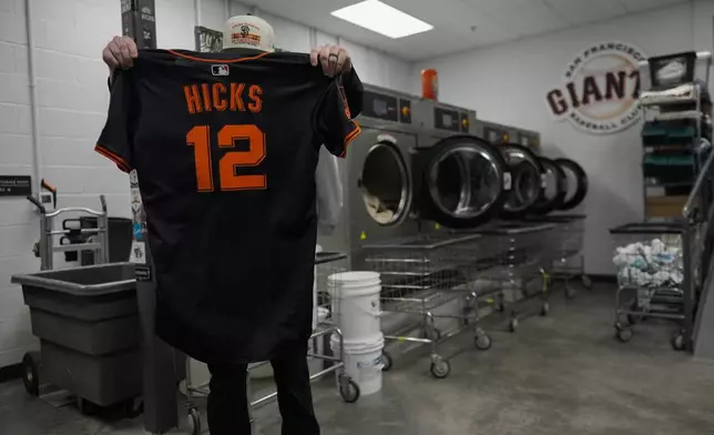 San Francisco Giants clubhouse attendant Riley Halpin inspects pitcher Jordan Hicks' jersey before putting it in the washing machine during baseball spring training at the team's facility, Monday, Feb. 17, 2025, in Scottsdale, Ariz. (AP Photo/Carolyn Kaster)