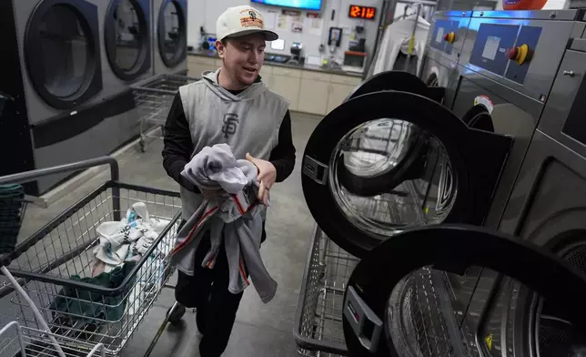San Francisco Giants clubhouse attendant Riley Halpin loads a washing machine during baseball spring training at the team's facility, Monday, Feb. 17, 2025, in Scottsdale, Ariz. (AP Photo/Carolyn Kaster)