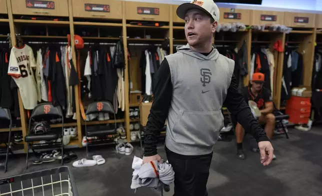 San Francisco Giants clubhouse attendant Riley Halpin gathers dirty clothes in the clubhouse after spring training baseball practice at the team's facility, Monday, Feb. 17, 2025, in Scottsdale, Ariz. (AP Photo/Carolyn Kaster)