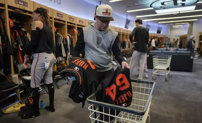 San Francisco Giants clubhouse attendant Riley Halpin gathers dirty clothes in the clubhouse after spring training baseball practice at the team's facility, Monday, Feb. 17, 2025, in Scottsdale, Ariz. (AP Photo/Carolyn Kaster)
