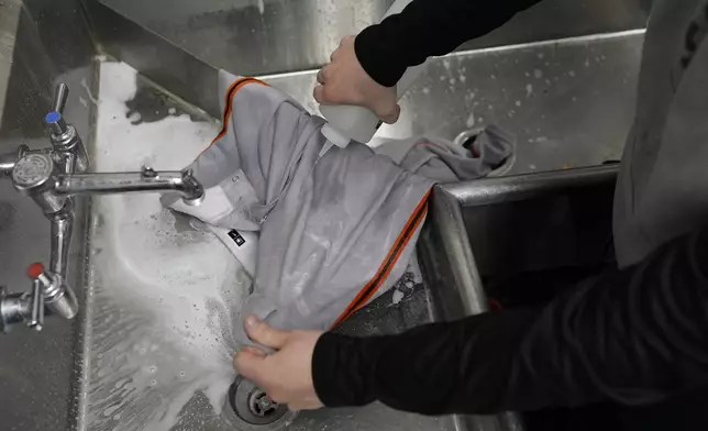 San Francisco Giants clubhouse attendant Riley Halpin removes stains from baseball pants in the laundry room sink during baseball spring training at the team's facility, Monday, Feb. 17, 2025, in Scottsdale, Ariz. (AP Photo/Carolyn Kaster)