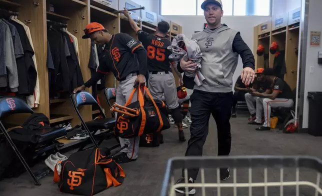 San Francisco Giants clubhouse attendant Riley Halpin gathers dirty clothes in the clubhouse after spring training baseball practice at the team's facility, Monday, Feb. 17, 2025, in Scottsdale, Ariz. (AP Photo/Carolyn Kaster)