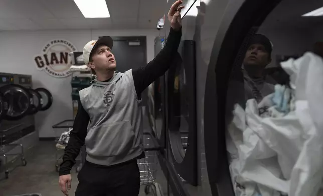 San Francisco Giants clubhouse attendant Riley Halpin starts a clothes dryer in the laundry room during baseball spring training at the team's facility, Monday, Feb. 17, 2025, in Scottsdale, Ariz. (AP Photo/Carolyn Kaster)