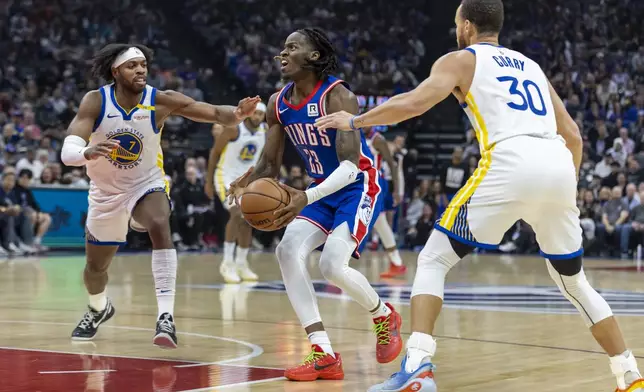 Sacramento Kings guard Keon Ellis (23) attempts a shot with Golden State Warriors guard Buddy Hield (7) and Golden State Warriors guard Stephen Curry (30) on defense during the first half of an NBA basketball game Friday, Feb. 21, 2025, in Sacramento, Calif. (AP Photo/Sara Nevis)