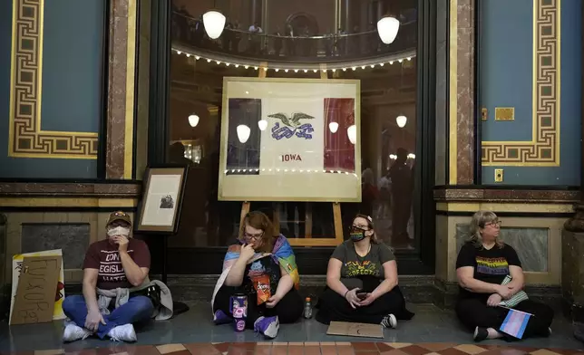 Protesters sit in the rotunda at the Iowa state Capitol to denounce a bill that would strip the state civil rights code of protections based on gender identity, Thursday, Feb. 27, 2025, in Des Moines, Iowa. (AP Photo/Charlie Neibergall)