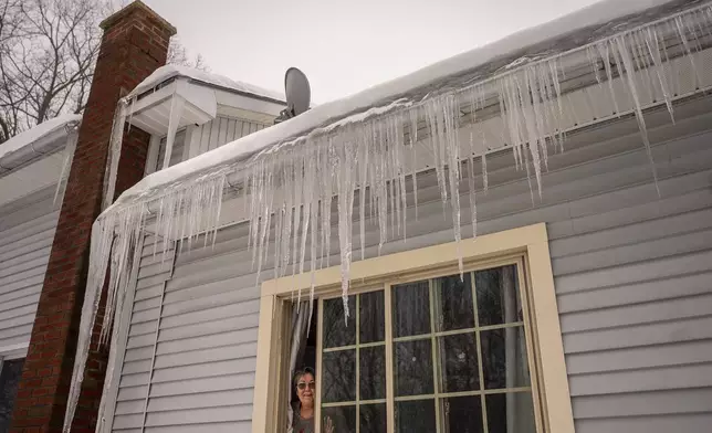 Claire Gagne peeks out from underneath an impressive curtain of icicles on her home in Lewiston, Maine, Thursday, Feb. 13, 2025. (Andree Kehn/Sun Journal via AP)