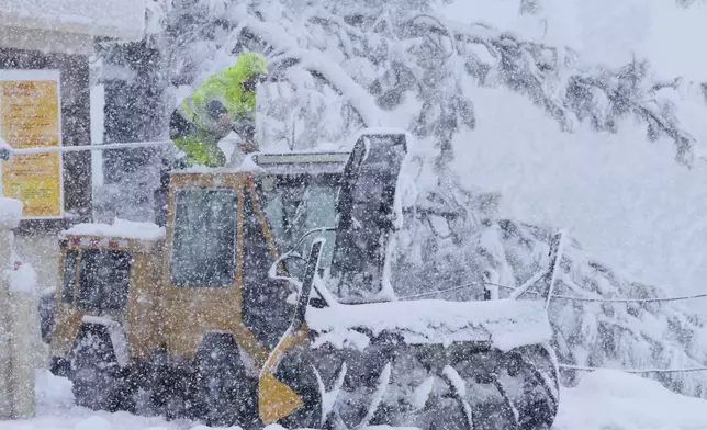 A person kneels on top of a plow tractor during a storm Thursday, Feb. 13, 2025, in Truckee, Calif. (AP Photo/Brooke Hess-Homeier)