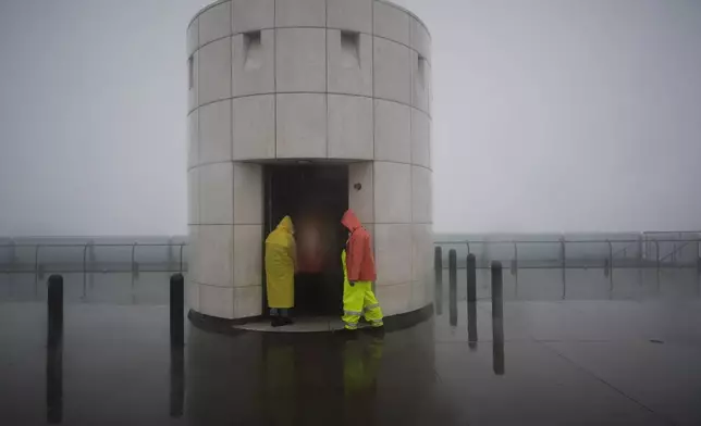 Workers shield themselves from the rain at the Griffith Park Observatory Thursday, Feb. 13, 2025, in Los Angeles. (AP Photo/Damian Dovarganes)