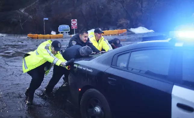 Police officers push an emergency vehicle stuck in mud in the Palisades Fire zone during a storm Thursday, Feb. 13, 2025, in Malibu, Calif. (AP Photo/Ethan Swope)