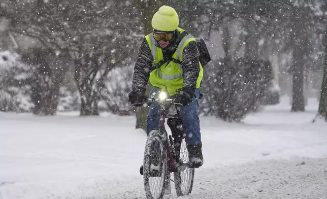 A biker makes their way on a street during a snowfall Wednesday, Feb. 12, 2025, in Shorewood, Wis. (AP Photo/Morry Gash)