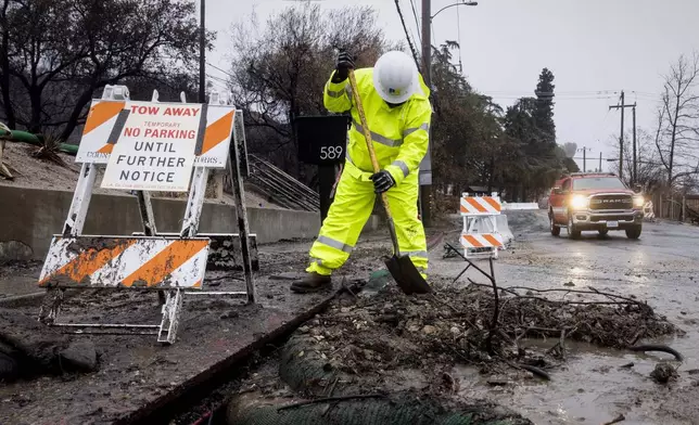A worker clears debris from a rain gutter in the Eaton Fire zone during a storm Thursday, Feb. 13, 2025, in Altadena, Calif. (AP Photo/Etienne Laurent)