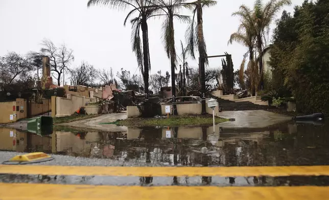 Water is reflected in front of a fire-ravaged property in the Palisades Fire zone during a storm Thursday, Feb. 13, 2025, in the Pacific Palisades neighborhood of Los Angeles. (AP Photo/Ethan Swope)