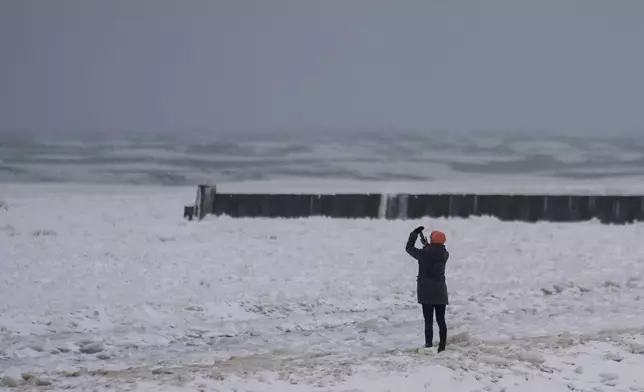A person takes pictures as they walk on a beach along the shore of Lake Michigan, Wednesday, Feb. 12, 2025, in Chicago. (AP Photo/Kiichiro Sato)