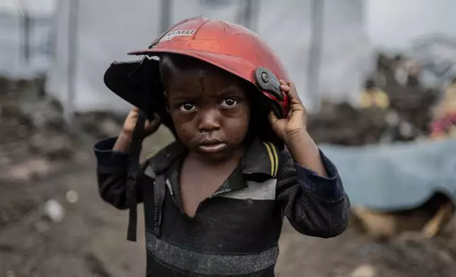 A child displaced by the fighting between M23 rebels and government soldiers holds a damaged helmet at the camp in Goma, Democratic Republic of the Congo, Tuesday, Feb. 11, 2025. (AP Photo/Moses Sawasawa)