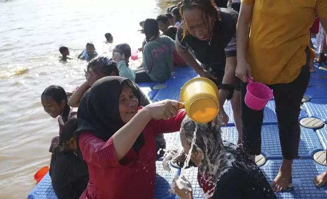 A woman pours water on another by the Cisadane River, ahead the holy fasting month of Ramadan in Tangerang, Indonesia, Friday, Feb 28, 2025. (AP Photo/Tatan Syuflana)