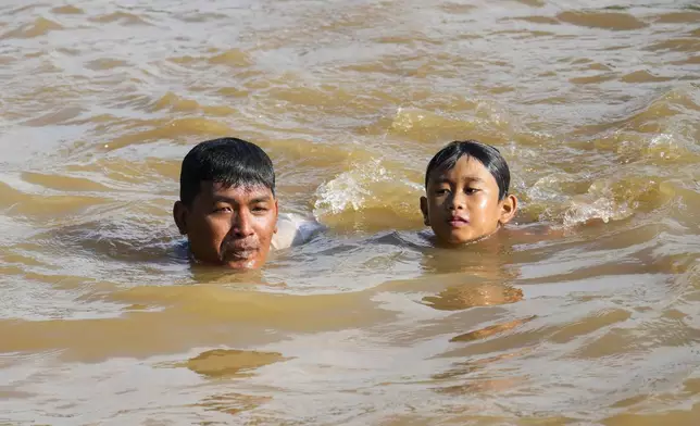 Samsul Anwar, left, and his nephew Argha al Khawarizmi swim in the Cisadane River, ahead the holy fasting month of Ramadan in Tangerang, Indonesia, Friday, Feb 28, 2025. (AP Photo/Tatan Syuflana)