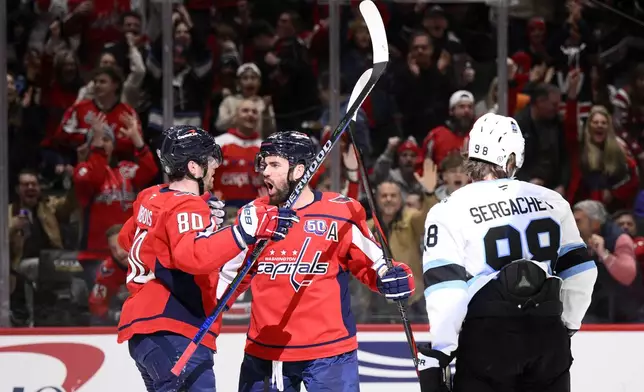 Washington Capitals right wing Tom Wilson, center, celebrates his goal with left wing Pierre-Luc Dubois (80) next to Utah Hockey Club defenseman Mikhail Sergachev (98) during the first period of an NHL hockey game, Sunday, Feb. 9, 2025, in Washington. (AP Photo/Nick Wass)