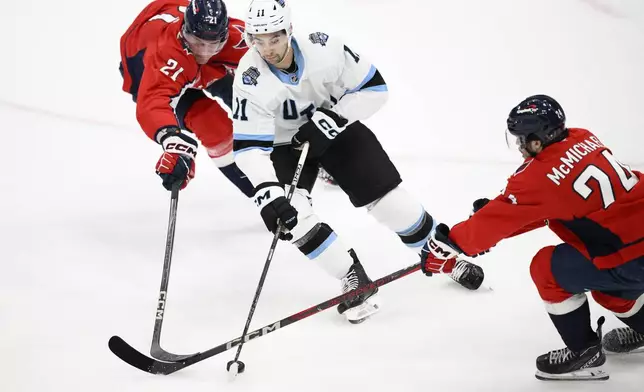 Utah Hockey Club right wing Dylan Guenther (11) battles for the puck against Washington Capitals center Aliaksei Protas (21) and center Connor McMichael (24) during overtime of an NHL hockey game, Sunday, Feb. 9, 2025, in Washington. (AP Photo/Nick Wass)