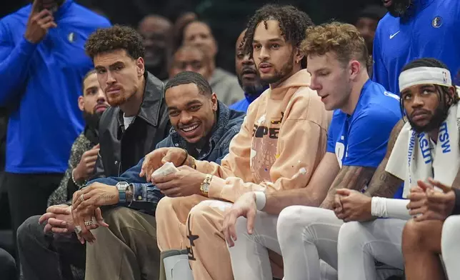 Dallas Mavericks players, from left, Caleb Martin, Dwight Powell, P.J. Washington and Dereck Lively II sit with teammates on the bench during the first half of an NBA basketball game against the Miami Heat Thursday, Feb. 13, 2025, in Dallas. (AP Photo/Julio Cortez)