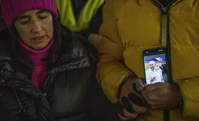 Faithful hold a smartphone with a picture of Pope Francis as they pray during a nightly rosary for his recovery in St. Peter's Square at The Vatican, Monday, Feb. 24, 2025. (AP Photo/Bernat Armangue)