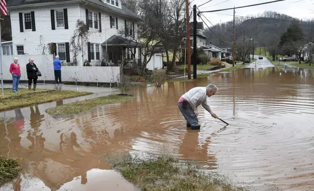Harry Miller works to open a clogged sewer drain near his house in Nitro, W.Va., as his neighbors look on Thursday, Feb. 6, 2025. (Chris Dorst/Charleston Gazette-Mail via AP)