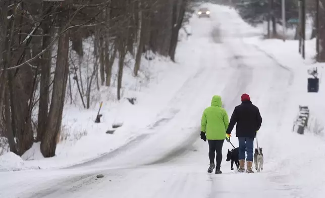 Molly, left, and Eric Bemis walk their dogs on a snow covered road, Thursday, Feb. 6, 2025, in East Derry, N.H. (AP Photo/Charles Krupa)
