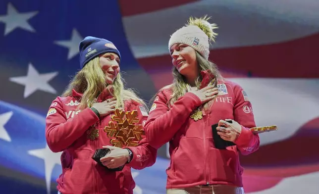 United States' Mikaela Shiffrin, left, and United States' Breezy Johnson listen to the national anthem as they wear their gold medals for a women's team combined event, at the Alpine Ski World Championships, in Saalbach-Hinterglemm, Austria, Tuesday, Feb. 11, 2025. (AP Photo/Giovanni Auletta)