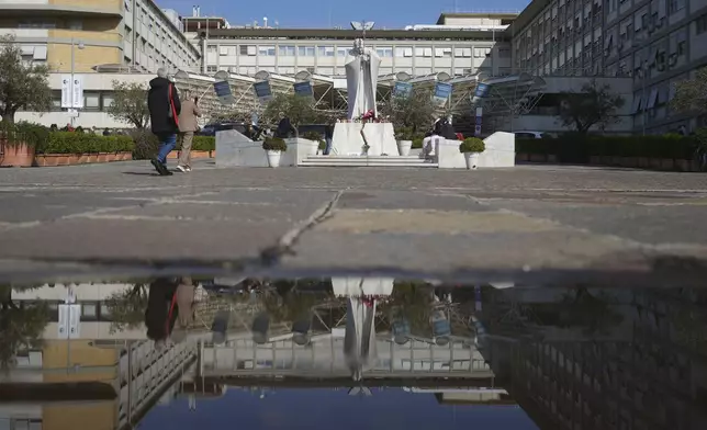The statue of Pope John Paul II in front of the Agostino Gemelli Polyclinic is reflected in a puddle, in Rome, Thursday, Feb. 20, 2025, as the Pontiff is hospitalised since Friday, Feb. 14. (AP Photo/Alessandra Tarantino)