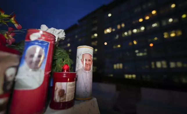 Candles with pictures of Pope Francis are laid under the statue of late Pope John Paul II outside Agostino Gemelli Polyclinic in Rome, Wednesday, Feb. 19, 2025, where the Pontiff is hospitalized since Friday, Feb. 14. (AP Photo/Andrew Medichini)