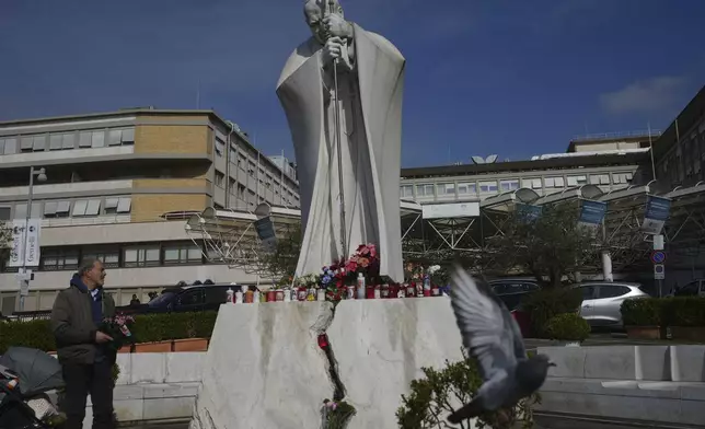A man carries flowers at the statue of Pope John Paul II in front of the Agostino Gemelli Polyclinic, in Rome, Thursday, Feb. 20, 2025, where the Pontiff is hospitalized since Friday, Feb. 14.(AP Photo/Alessandra Tarantino)