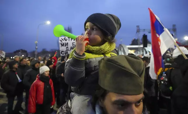 A man wearing a traditional Serbian hat with a child attends a student-led large protest and a 15-hour blockade of the streets in Serbian industrial town of Kragujevac, to protest the deaths of 15 people killed in the November collapse of a train station canopy, Saturday, Feb. 15, 2025. (AP Photo/Darko Vojinovic)
