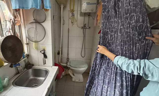 Housewife Jimmy Au pulls back a curtain to reveal her toilet at home in a residential area of Prince Edward district in Hong Kong, on Jan. 21, 2025. (AP Photo/Kanis Leung)