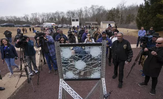 People inspect a sample of the material used in bullet-resistant enclosures to be installed on buses, after it was fired pond during a demonstration at a range in Bedminster, Pa., Tuesday, Feb. 25, 2025. (AP Photo/Matt Rourke)