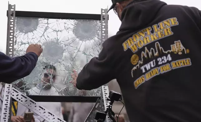 People inspect a sample of the material used in bullet-resistant enclosures to be installed on buses, after it was fired pond during a demonstration at a range in Bedminster, Pa., Tuesday, Feb. 25, 2025. (AP Photo/Matt Rourke)