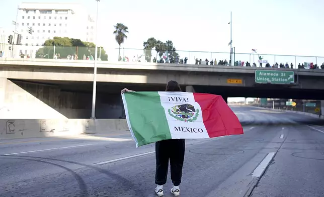A demonstrator holds a Mexican flag while standing on the 110 freeway during a protest calling for immigration reform Sunday, Feb. 2, 2025, in Los Angeles. (AP Photo/Eric Thayer)