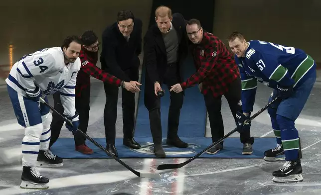 Second from left to right, Team Canada Invictus athlete Lee Jarrat, Vancouver Canucks owner Francesco Aquilini, Prince Harry, the Duke of Sussex, and Team Canada Invictus athlete Andre Crocker drop the puck for Toronto Maple Leafs' Auston Matthews (34) and Canucks' Tyler Myers (57) prior to an NHL hockey game in Vancouver, British Columbia, Saturday, Feb. 8, 2025. (Ethan Cairns/The Canadian Press via AP)