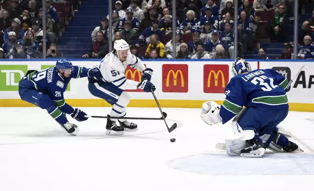 Vancouver Canucks' Marcus Pettersson (29) lifts Toronto Maple Leafs' Philippe Myers' (51) stick as Canucks goaltender Kevin Lankinen (32) watches during the first period of an NHL hockey game in Vancouver, British Columbia, Saturday, Feb. 8, 2025. (Ethan Cairns/The Canadian Press via AP)