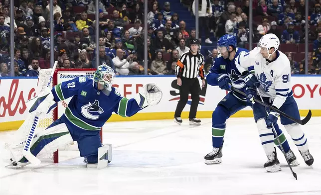 Vancouver Canucks goaltender Kevin Lankinen (32) stops the puck as Canucks' Derek Forbort (27) and Toronto Maple Leafs' John Tavares (91) watch during the second period of an NHL hockey game in Vancouver, British Columbia, Saturday, Feb. 8, 2025. (Ethan Cairns/The Canadian Press via AP)